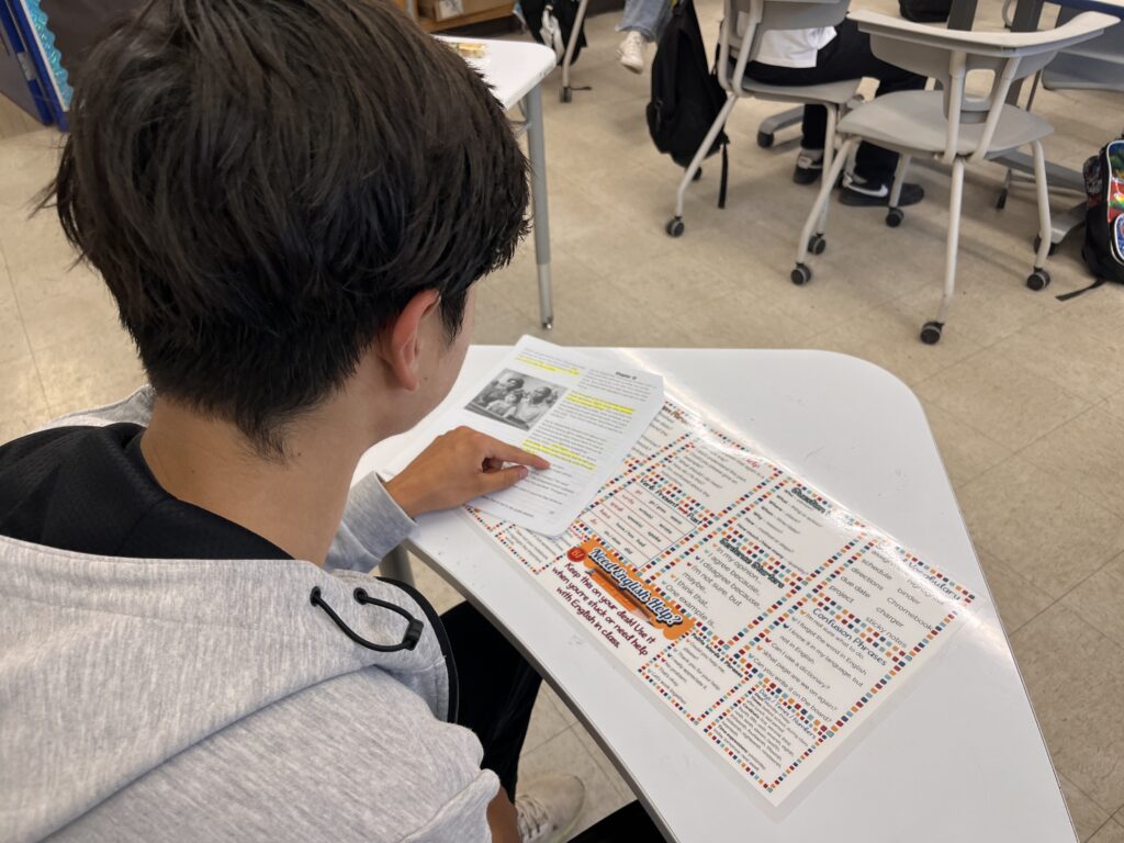 Teen ESL student using a laminated Survival English Desk Mat while reading a highlighted worksheet in class.