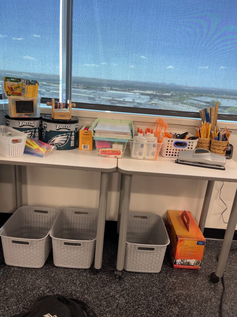 Organized ESL classroom supply station with baskets, pencils, glue, scissors, paper, rulers, and storage bins