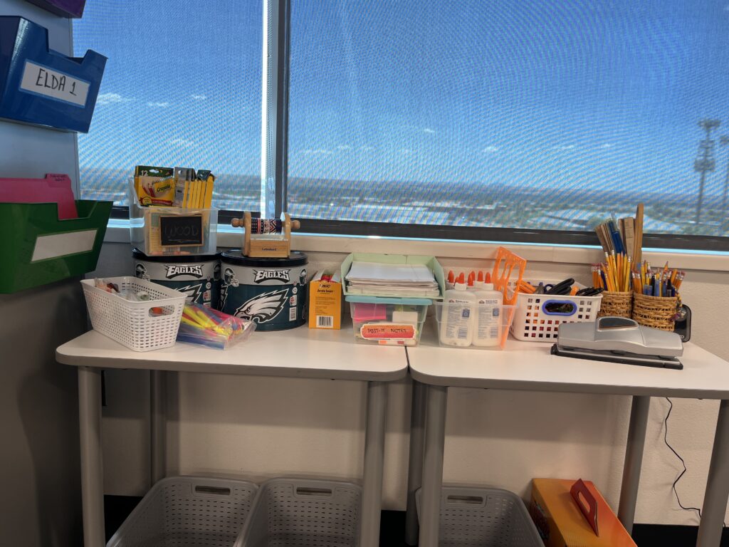 Organized high school ESL classroom supply station with pencils, glue, scissors, and storage baskets