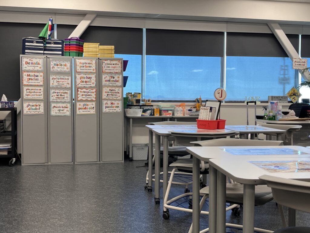High school ESL classroom with Spanish-English survival phrases, organized supplies, and group seating